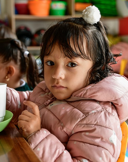 Una niña con abrigo rosa en un aula infantil